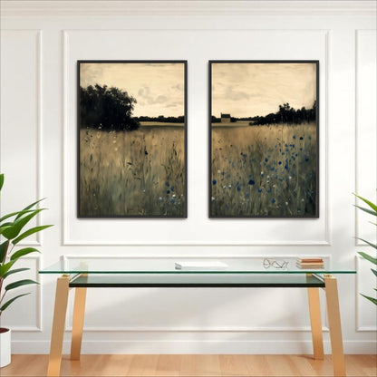 two framed paintings of a field with tall grass and trees, hanging on a white wall above a glass desk with a computer monitor and other office supplies.