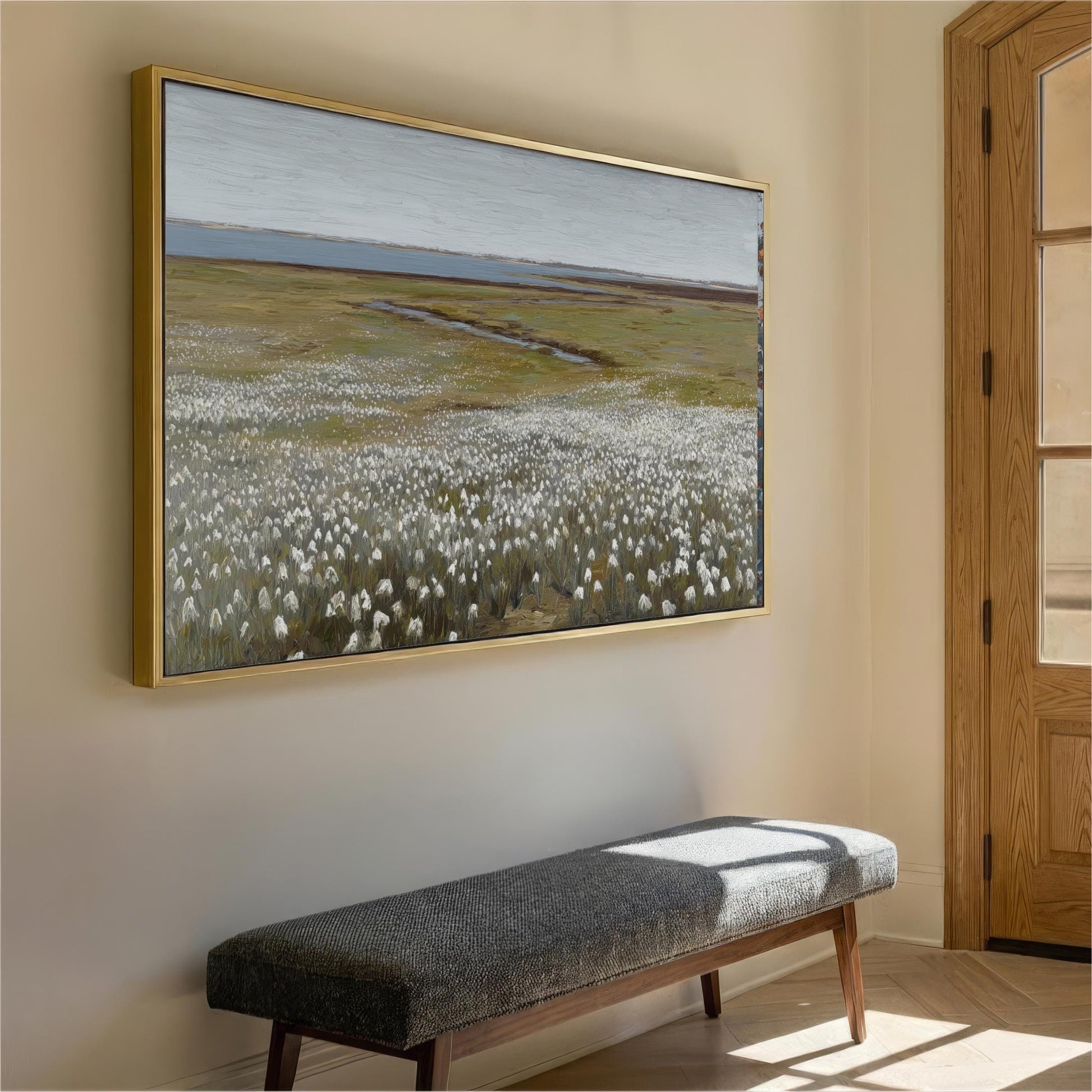 a large painting of a field with white flowers hanging on a wall, accompanied by a gray bench in the foreground.