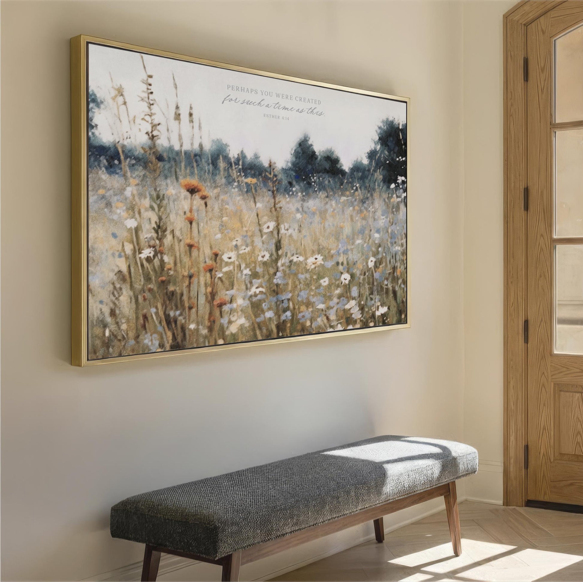 a large framed painting of a field of flowers hanging on a wall, with a gray bench placed in front of it.