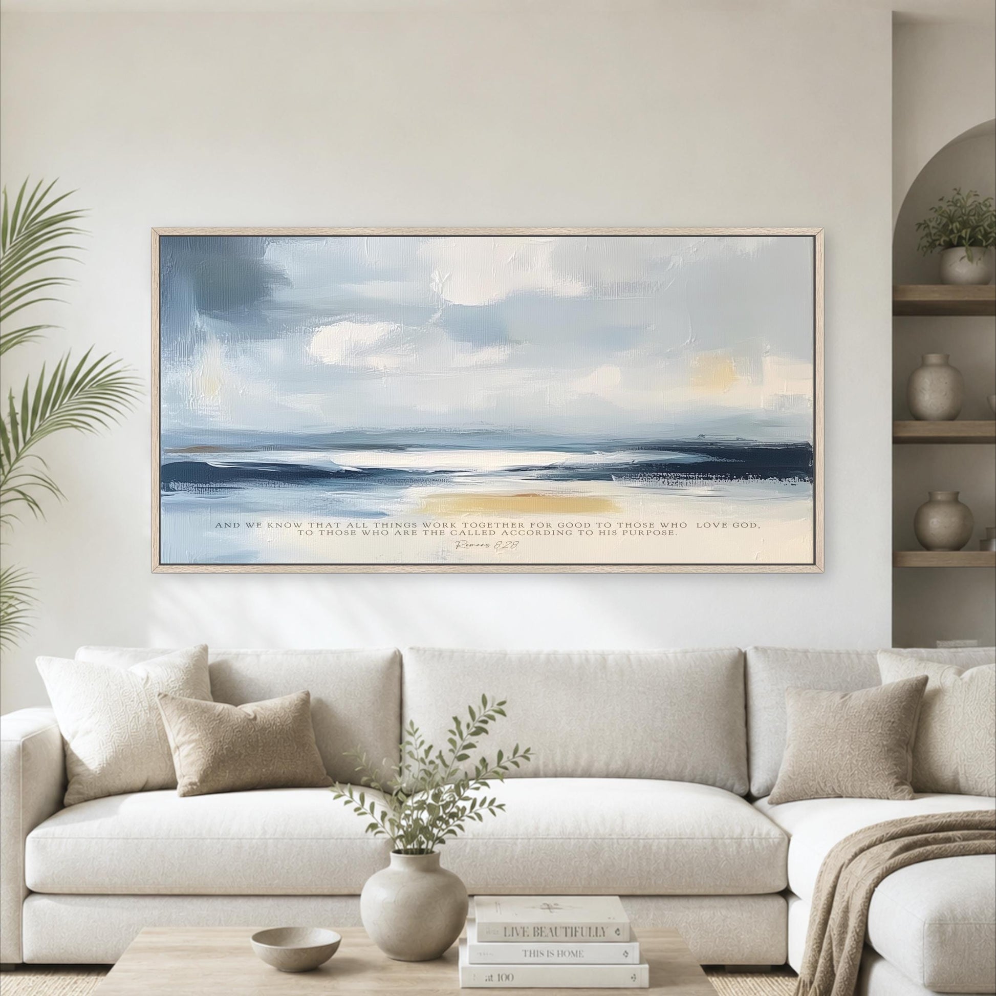 a large, framed painting of a serene landscape with a blue sky, clouds, and a sandy beach, hanging on a wall above a white couch in a living room setting.