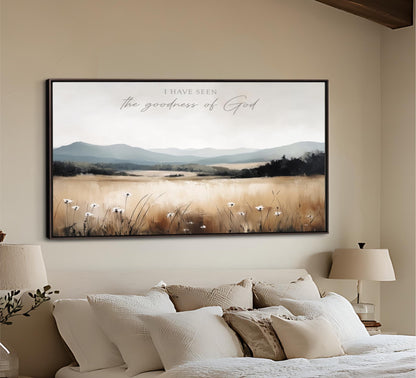 a large framed painting of a serene landscape with a field of flowers and mountains in the background, hanging on a wall above a bed with white pillows and a beige headboard.