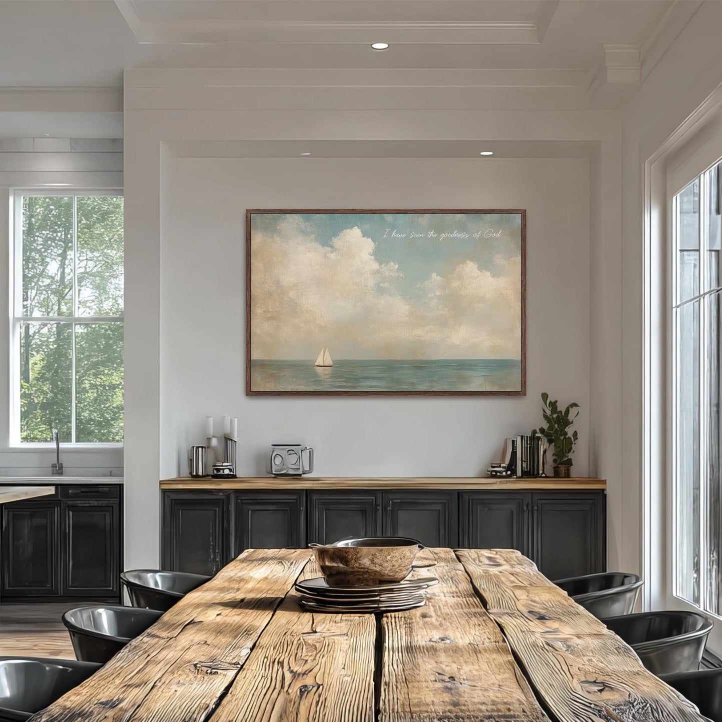 a dining room with a large wooden table surrounded by black chairs. Above the table, there is a framed painting depicting a sailboat on the ocean. The painting is hung on a white wall, and the dining table is set with a bowl and a plate.