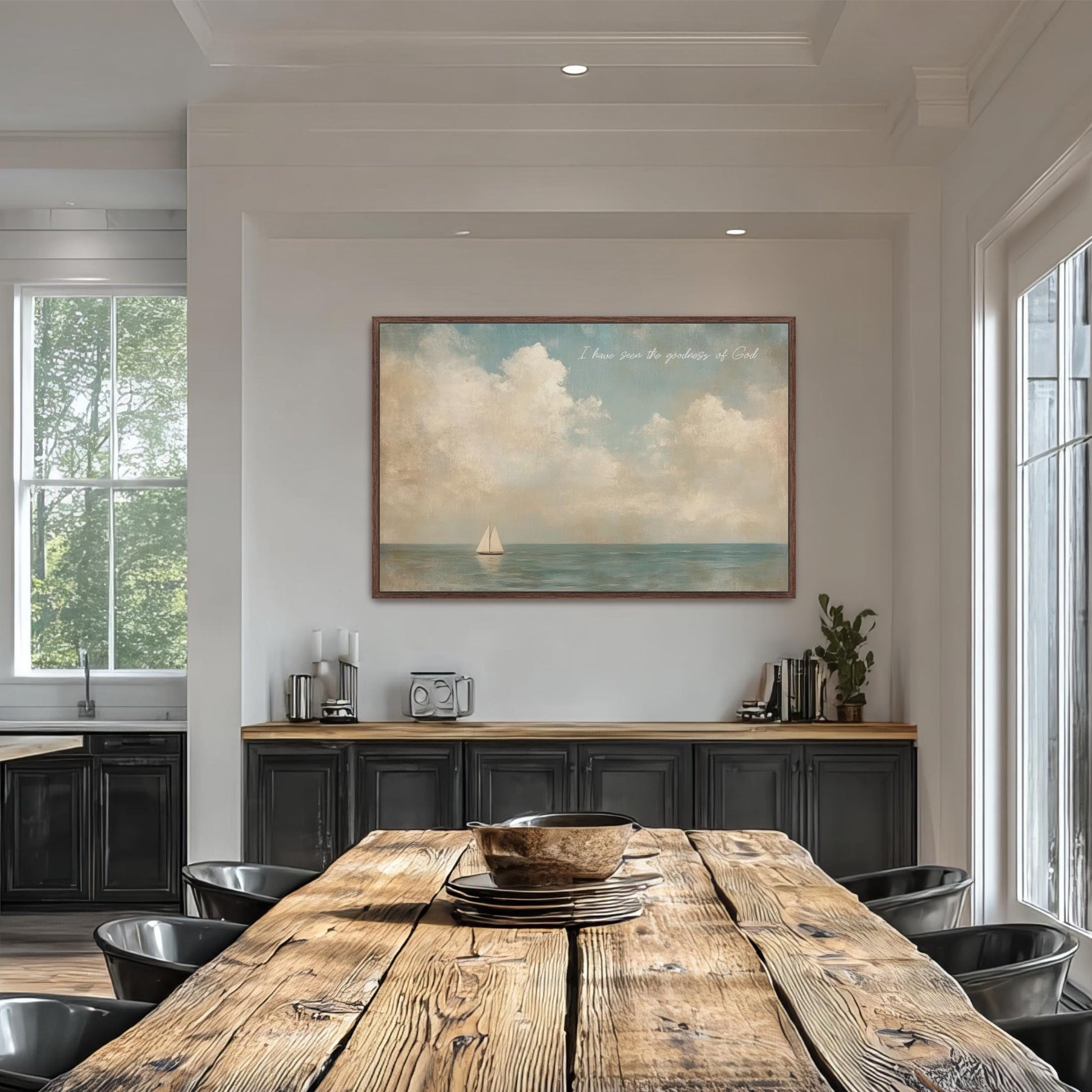 a dining room with a large wooden table surrounded by black chairs. Above the table, there is a framed painting depicting a sailboat on the ocean. The painting is hung on a white wall, and the dining table is set with a bowl and a plate.