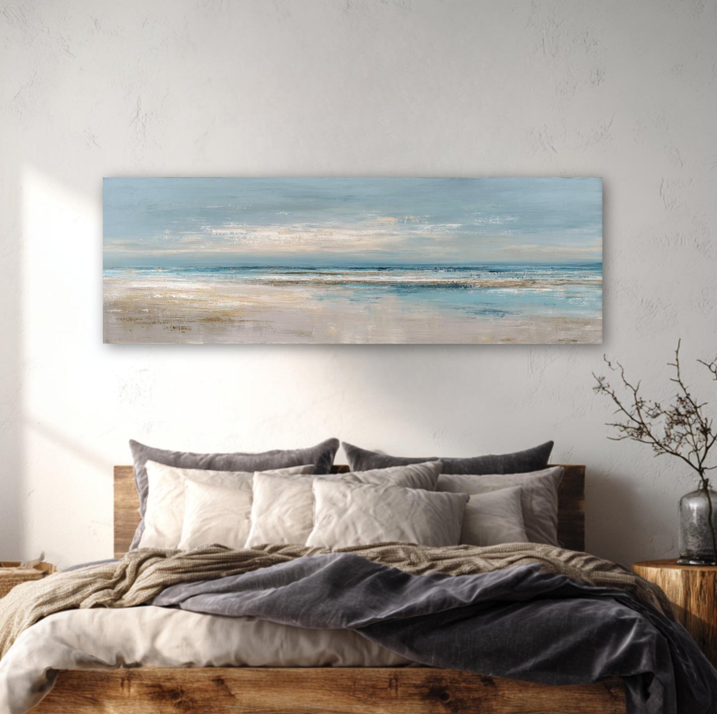 a large bedroom with a wooden bed frame, a painting of a beach scene hanging above it, and a vase of branches on a side table.