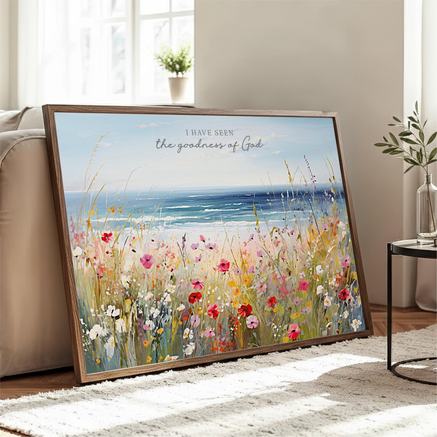 A framed painting depicting a vibrant field of colorful flowers, with a serene body of water in the background, is displayed on a wooden floor in a living room.