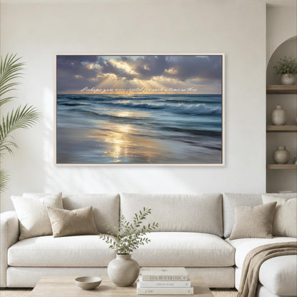 a large framed painting of a serene beach scene with waves crashing against the shore, set against a backdrop of a cloudy sky. The painting is hung on a wall above a white sofa, which is positioned in front of a coffee table. The room also includes a potted plant, a vase with greenery, and a bookshelf with decorative items.