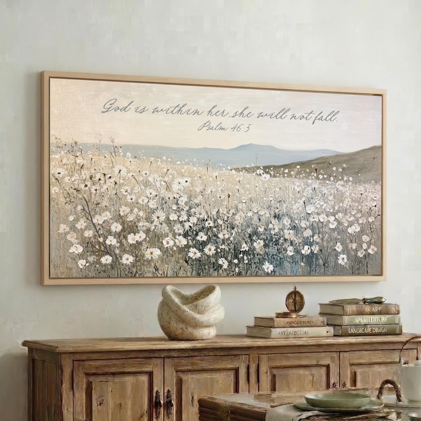 a framed painting of a field of flowers hanging on a wall above a wooden cabinet. The cabinet has a stack of books on top of it.