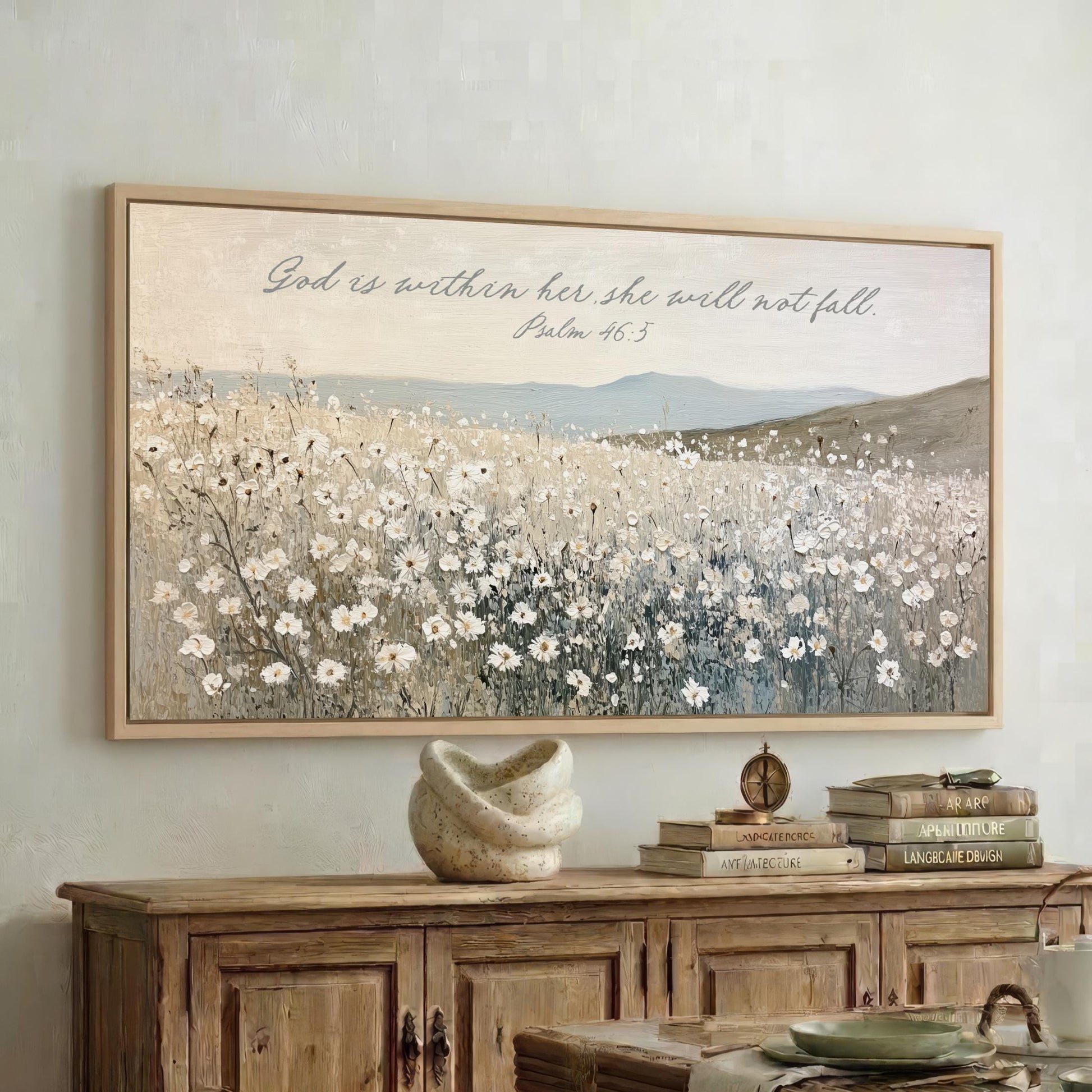 a framed painting of a field of flowers hanging on a wall above a wooden cabinet. The cabinet has a stack of books on top of it.