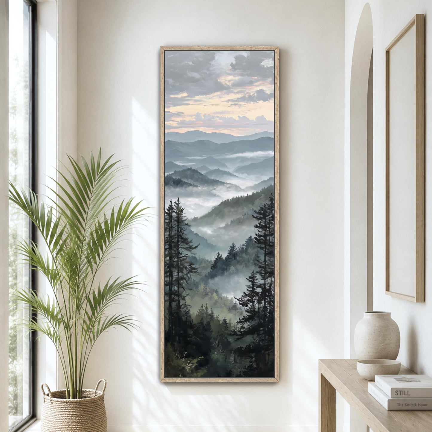 a large framed landscape painting hanging on a wall, depicting a mountainous, forested scene with a cloudy sky.