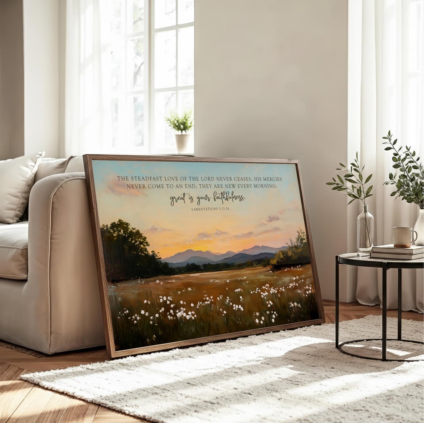 a large framed painting of a serene landscape with a field of flowers and mountains in the background, placed on a white rug in a living room setting.