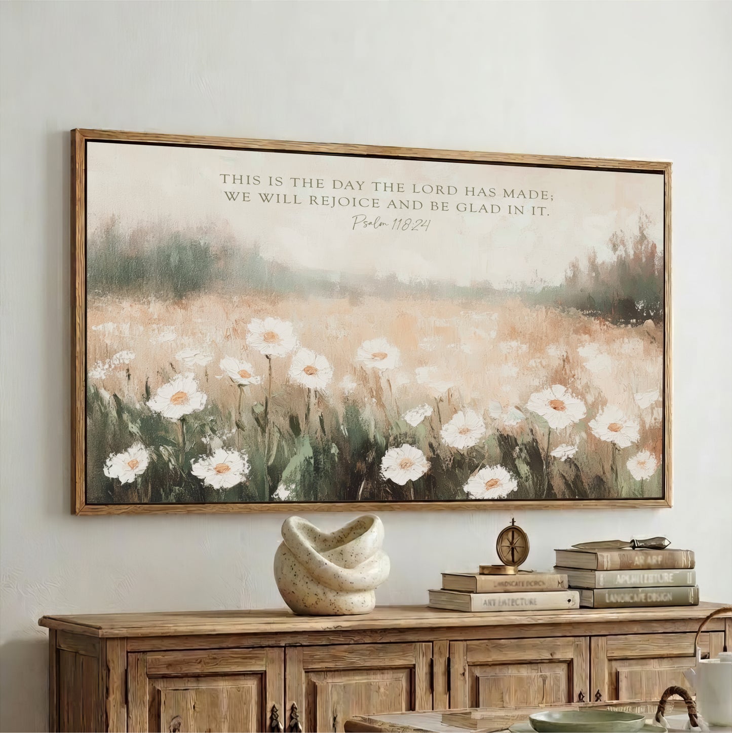 a large framed painting of a field of white flowers hanging on a wall above a wooden cabinet.