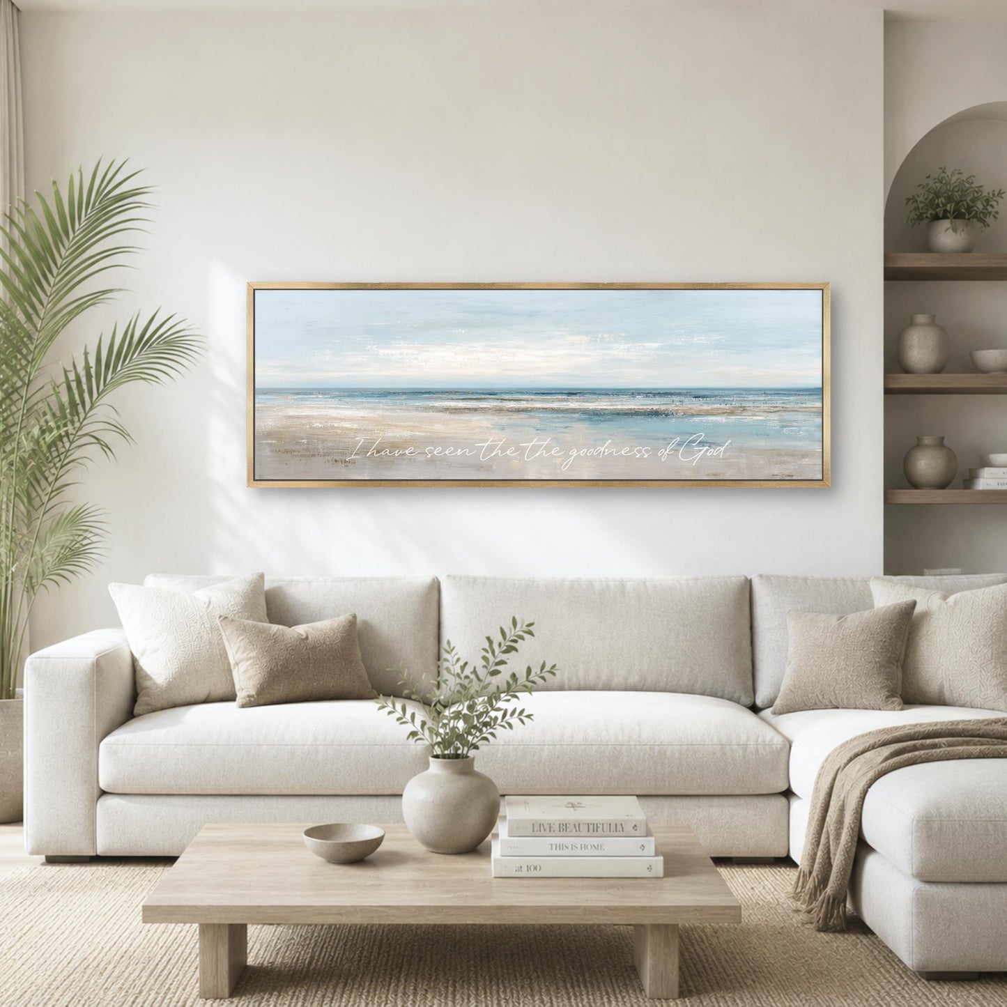 A living room with a large white sofa, a wooden coffee table, and a framed painting of a beach scene hanging on the wall above the sofa.