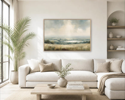 a serene living room with a large painting of a landscape hanging on the wall above a white sofa. The room is decorated with a potted plant, a vase with greenery, and a wooden coffee table with books and a bowl on it.