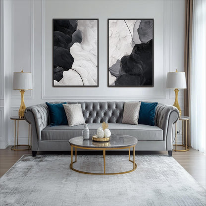 a modern living room with a gray tufted sofa, a round glass coffee table, and two gold side tables with lamps. Above the sofa, there are two abstract paintings on the wall, creating a stylish and sophisticated atmosphere.