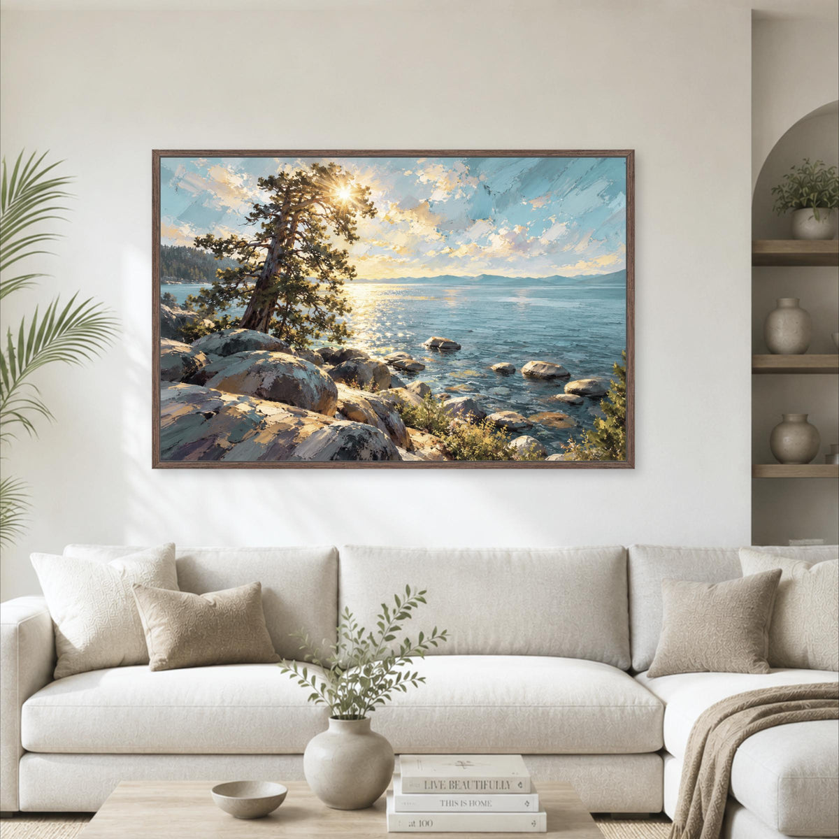 a large framed painting of a serene landscape with a rocky shore, a tree, and a body of water, hanging on a wall above a white sofa in a living room setting.