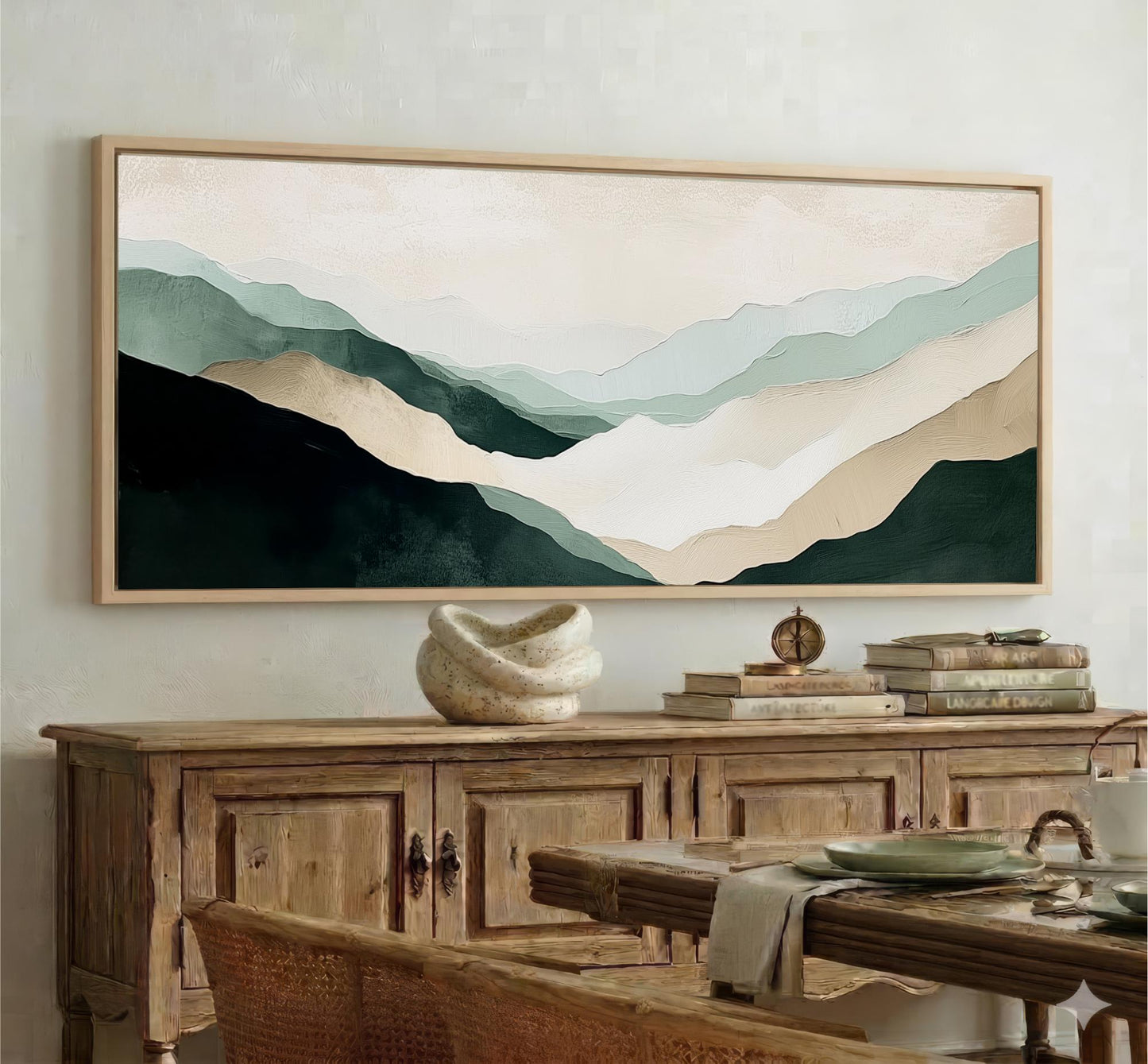 a large framed painting of mountains hanging on a wall above a wooden cabinet. The painting has a soothing color palette of green, blue, and beige, creating a serene and calming atmosphere in the room.