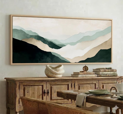 a large framed painting of mountains hanging on a wall above a wooden cabinet. The painting has a soothing color palette of green, blue, and beige, creating a serene and calming atmosphere in the room.