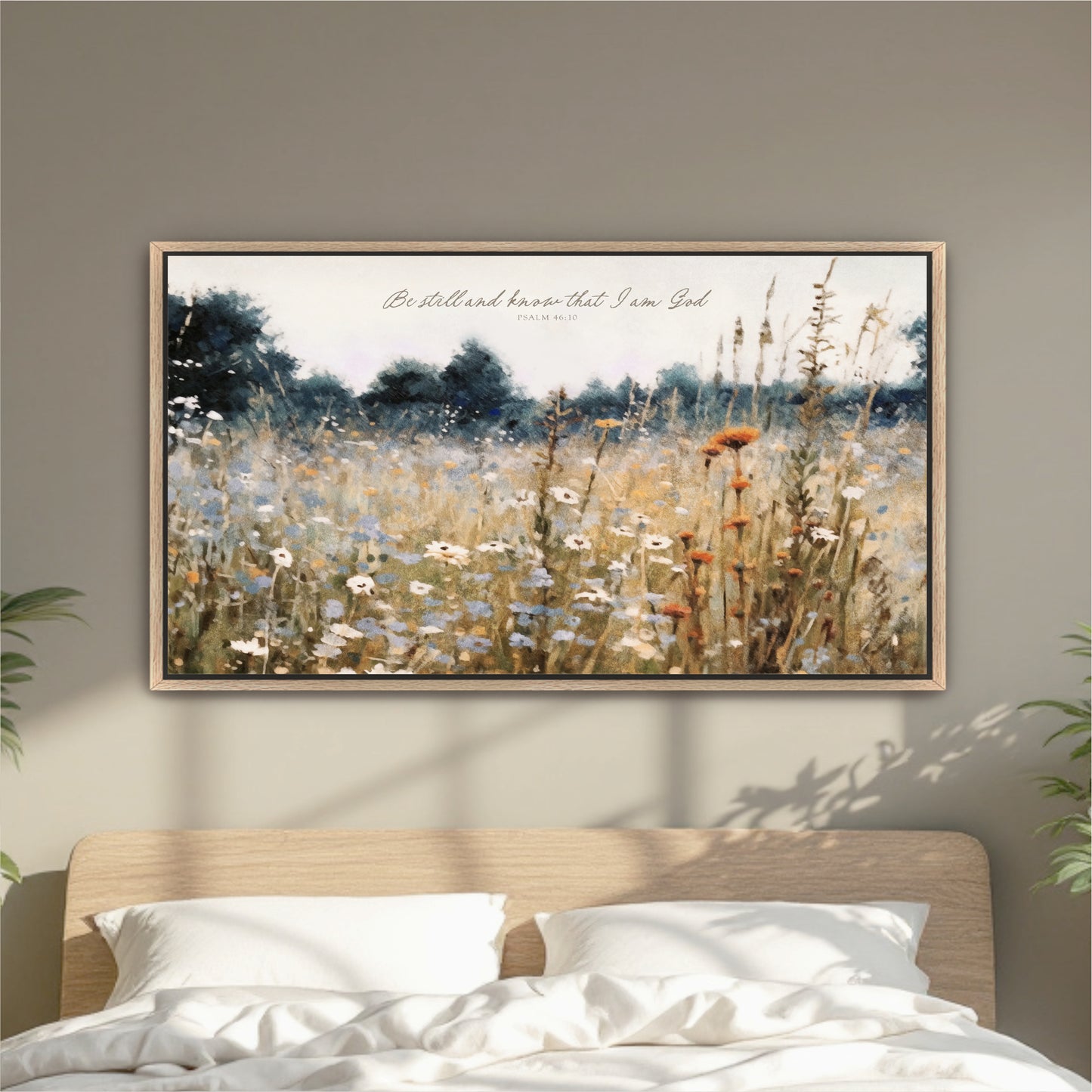a framed painting of a field of wildflowers hanging on a wall above a bed with white pillows.