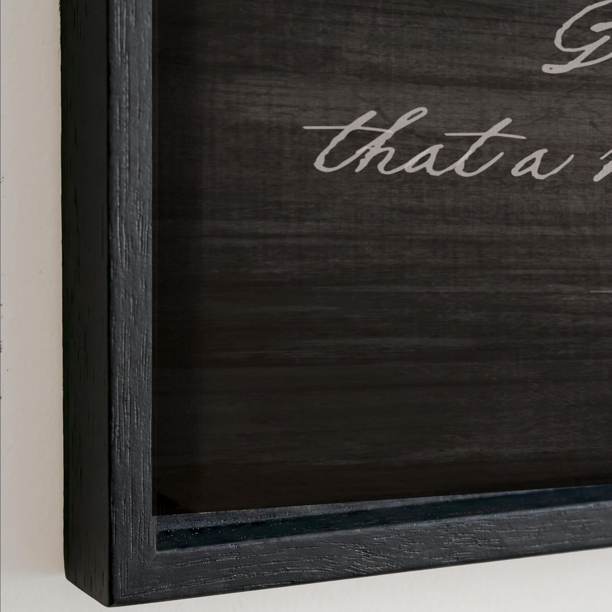 The image is a black and white photograph of a framed piece of art with a dark background and a white text overlay.