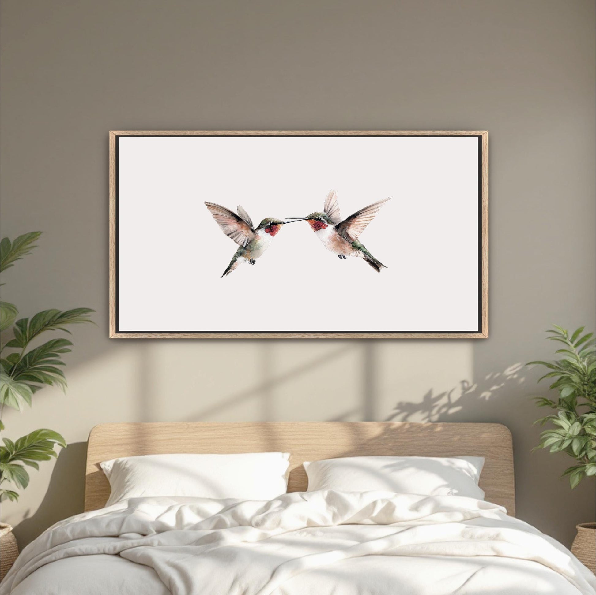 a framed picture of two hummingbirds on a white background, hanging on a wall above a bed with white bedding.