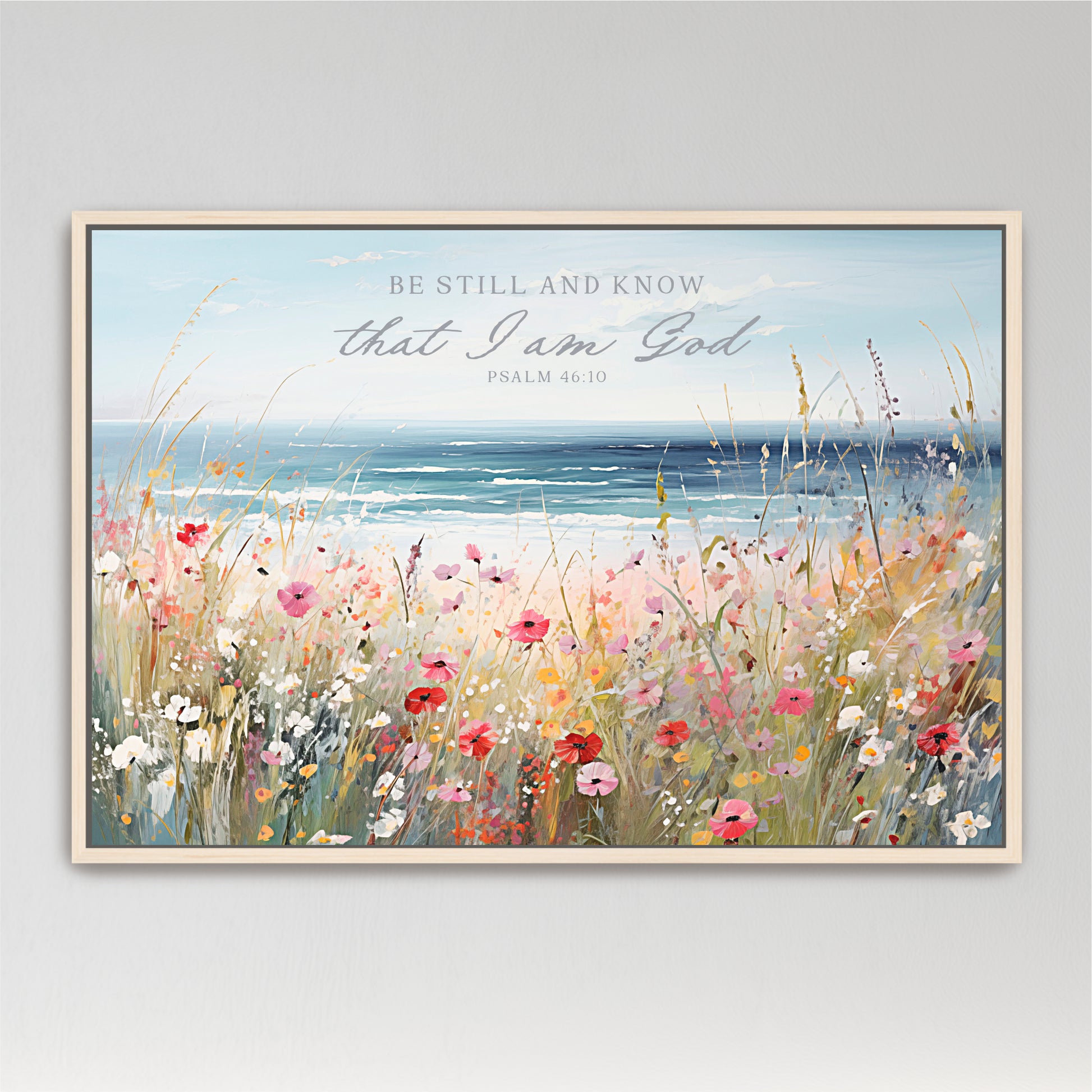 The image is a framed painting depicting a serene landscape with a field of colorful wildflowers in the foreground and a body of water in the background. The text overlay reads "Be Still and Know that I am God" from Psalm 46:10.