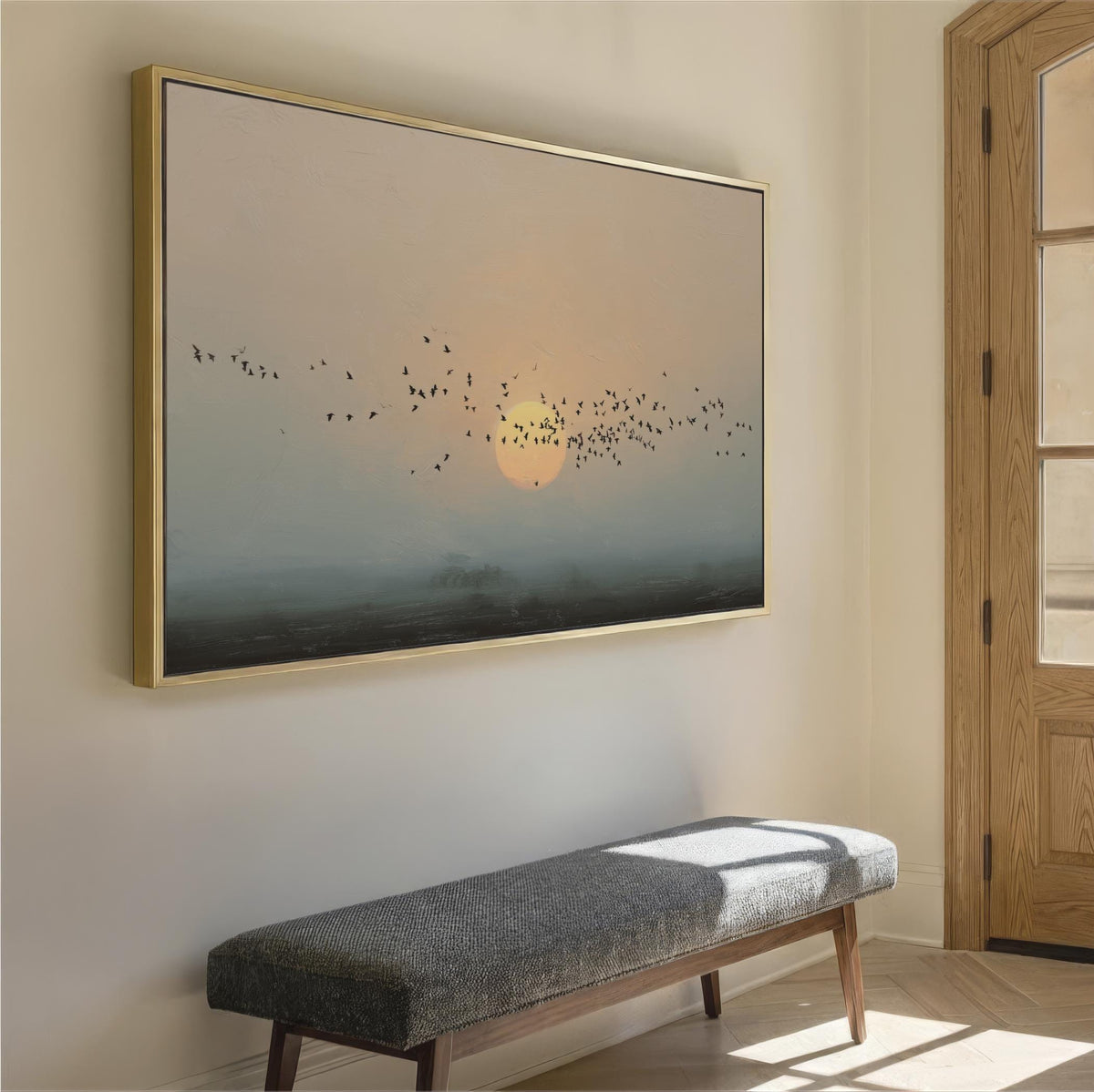 a large painting of a flock of birds flying over a landscape, with a warm sunset in the background. The painting is hung on a wall above a gray bench, creating a serene and peaceful atmosphere in the room.