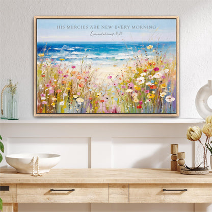 a framed painting of a vibrant field of flowers, with a serene ocean view in the background. The painting is hung on a wall above a wooden dresser, which has a white bowl and a vase on it. The painting is titled "His Mercies are New Every Morning" and includes a Bible verse from the book of Proverbs.