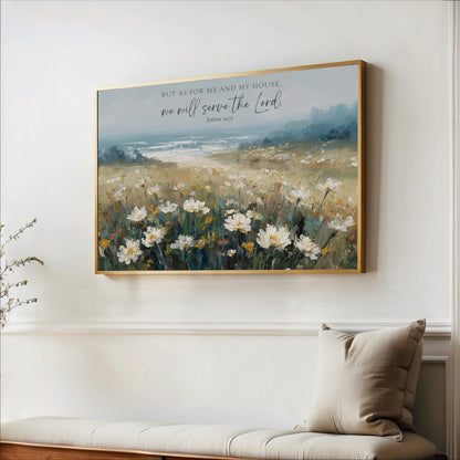 A framed painting of a field of white flowers hangs on a white wall, with a quote from the Bible above it.