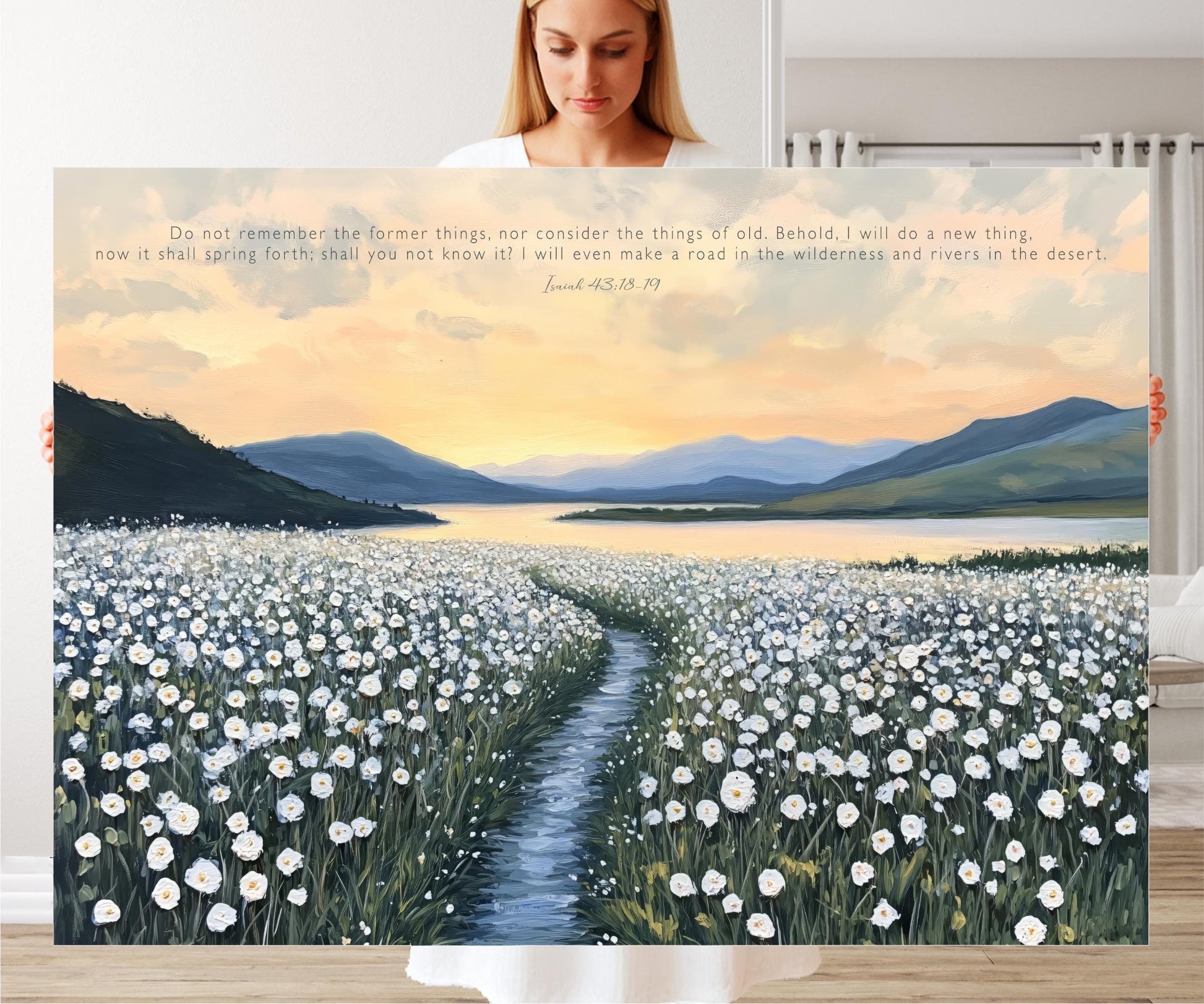 A woman stands in front of a large painting depicting a field of white flowers with a winding path leading through it, set against a backdrop of mountains and a sunset sky.