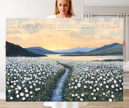 A woman stands in front of a large painting depicting a field of white flowers with a winding path leading through it, set against a backdrop of mountains and a sunset sky.