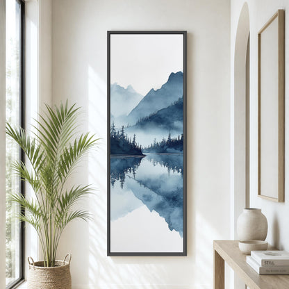 a large framed painting of a serene landscape with mountains, trees, and a lake, hanging on a wall in a room with a potted plant and a wooden table.