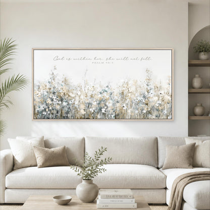 A living room with a large framed print of a floral landscape hanging on the wall above a white sofa. The print features a variety of flowers in different shades of white, blue, and green. The sofa is adorned with throw pillows and a vase of greenery. The room also includes a coffee table with books and decorative items, creating a cozy and inviting atmosphere.