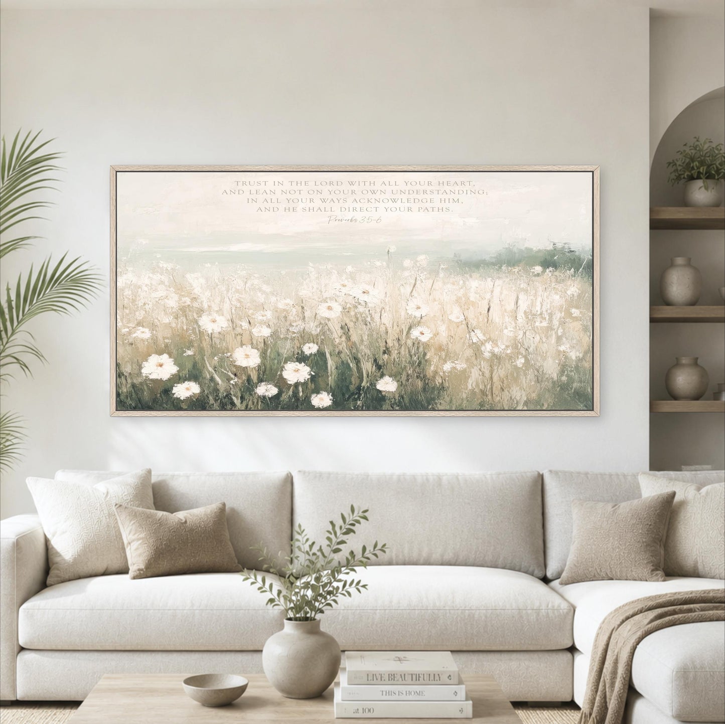a large framed painting of a field of white flowers hanging on a wall above a white sofa in a living room.
