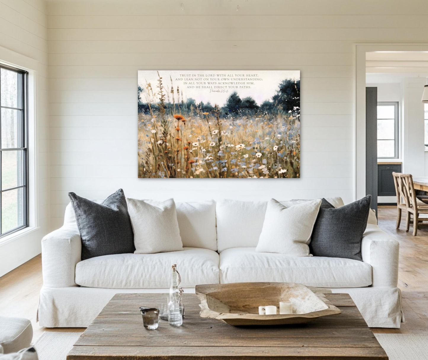 a living room with a white sofa, a wooden coffee table, and a painting of a field with flowers hanging on the wall above the sofa.