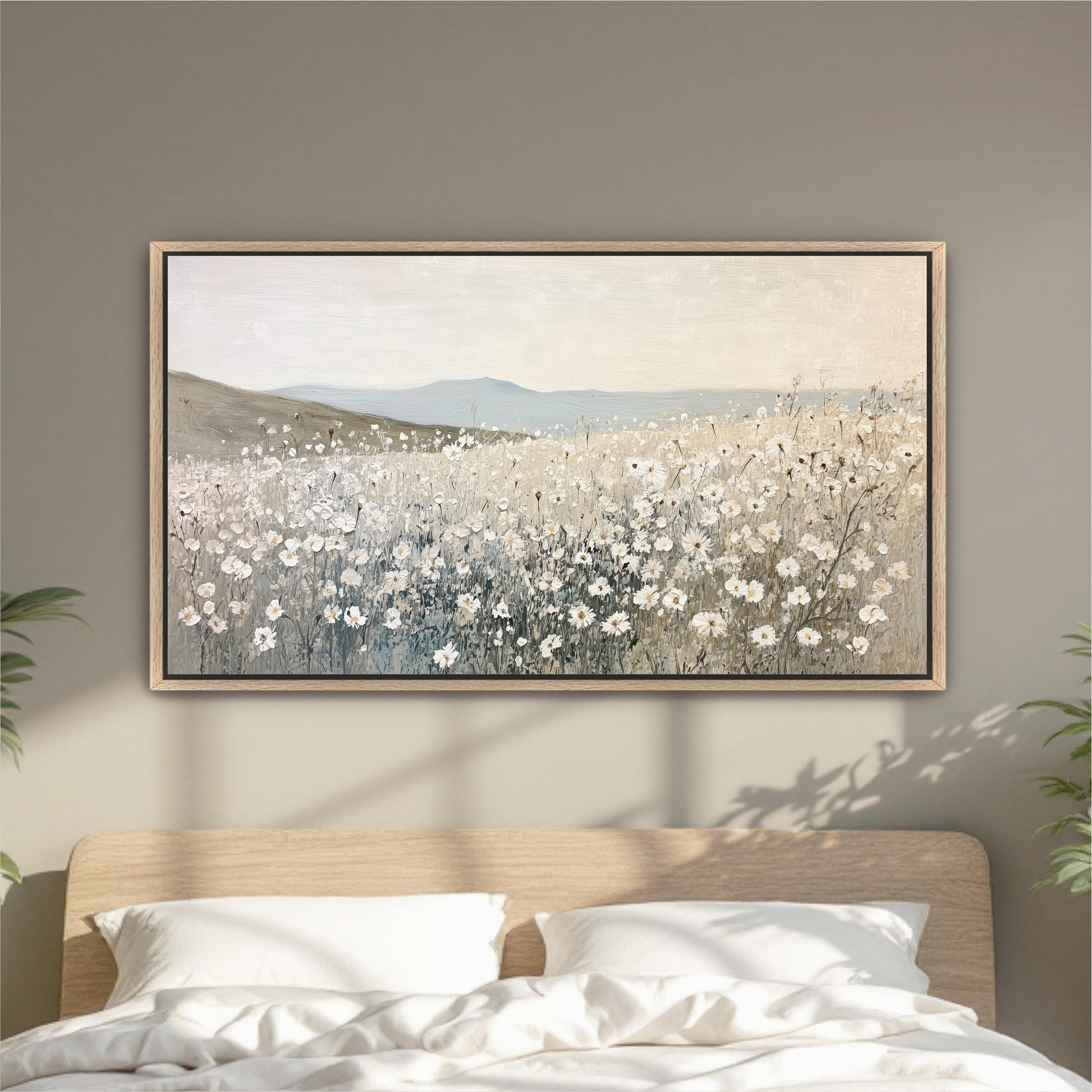 a large painting of a field of white flowers hanging on a wall above a bed with white pillows.