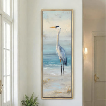 a large framed painting of a tall bird standing on a beach, with the ocean in the background.