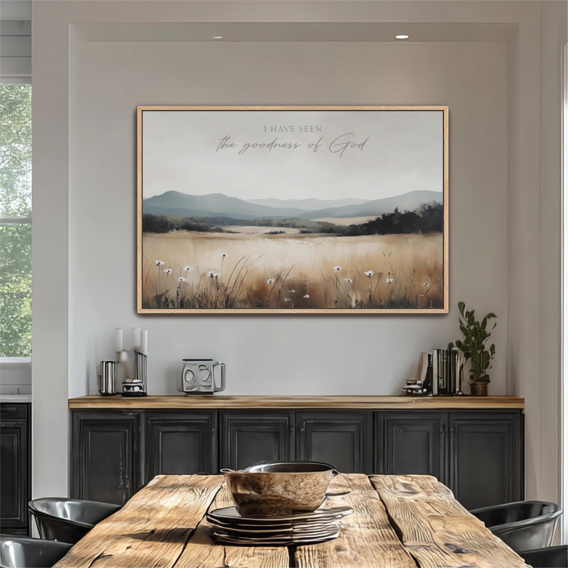 a large framed painting of a field with mountains in the background, hanging on a wall above a wooden dining table with chairs.