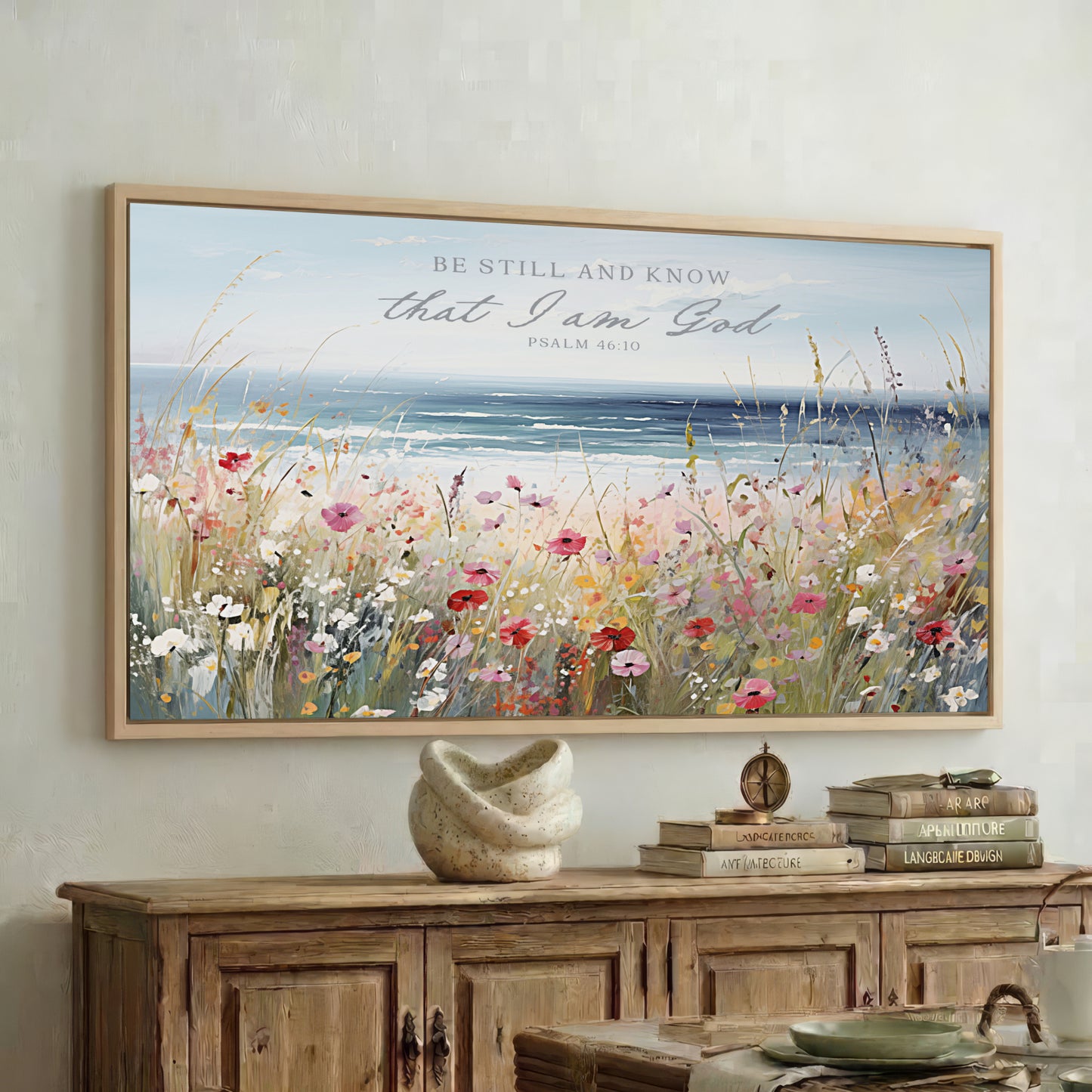 a large framed painting of a field of flowers hanging on a wall above a wooden cabinet.