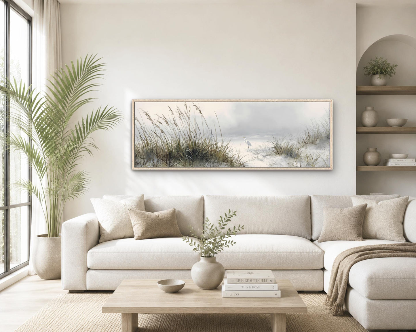 a serene living room with a large window, a white sofa, a wooden coffee table, and a framed landscape painting of a beach scene.