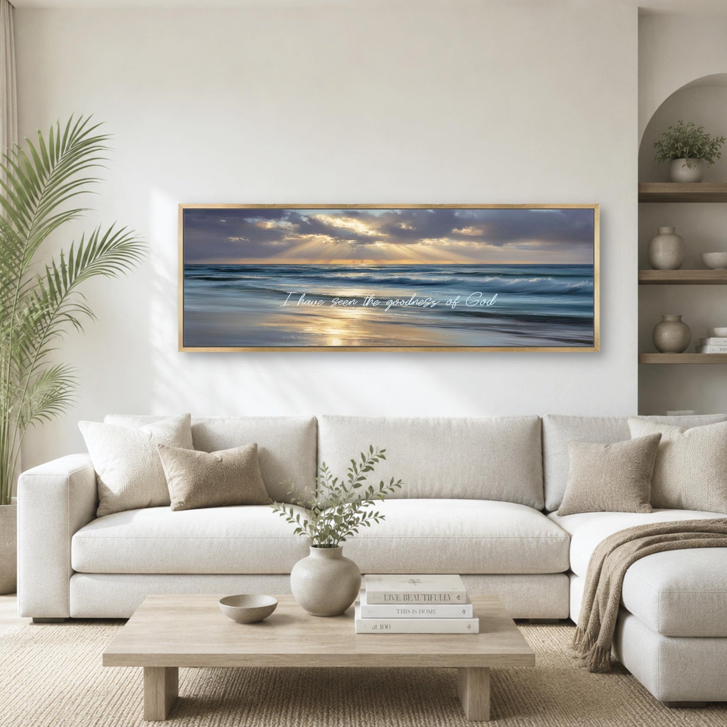 a large framed painting of a serene beach scene with a sunset over the ocean, hanging on a white wall above a white sofa in a living room.