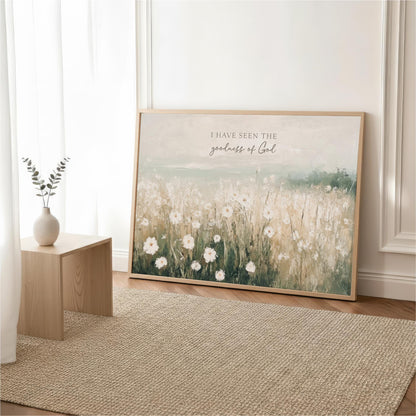 a large framed painting of a field of white flowers, with a vase of greenery on a small wooden table in the foreground.
