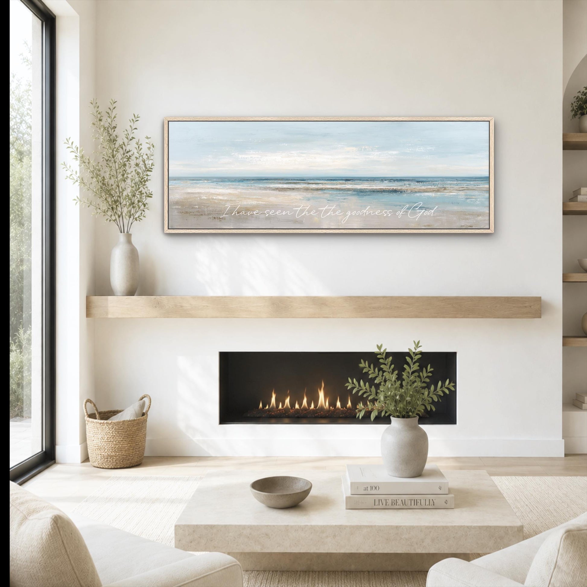 a cozy living room with a fireplace, a coffee table, and a framed landscape painting above it. The painting features a serene beach scene with a clear blue sky and calm ocean. The room is decorated with a vase of greenery, a woven basket, and a stack of books.