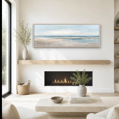a cozy living room with a fireplace, a coffee table, and a framed landscape painting above it. The painting features a serene beach scene with a clear blue sky and calm ocean. The room is decorated with a vase of greenery, a woven basket, and a stack of books.
