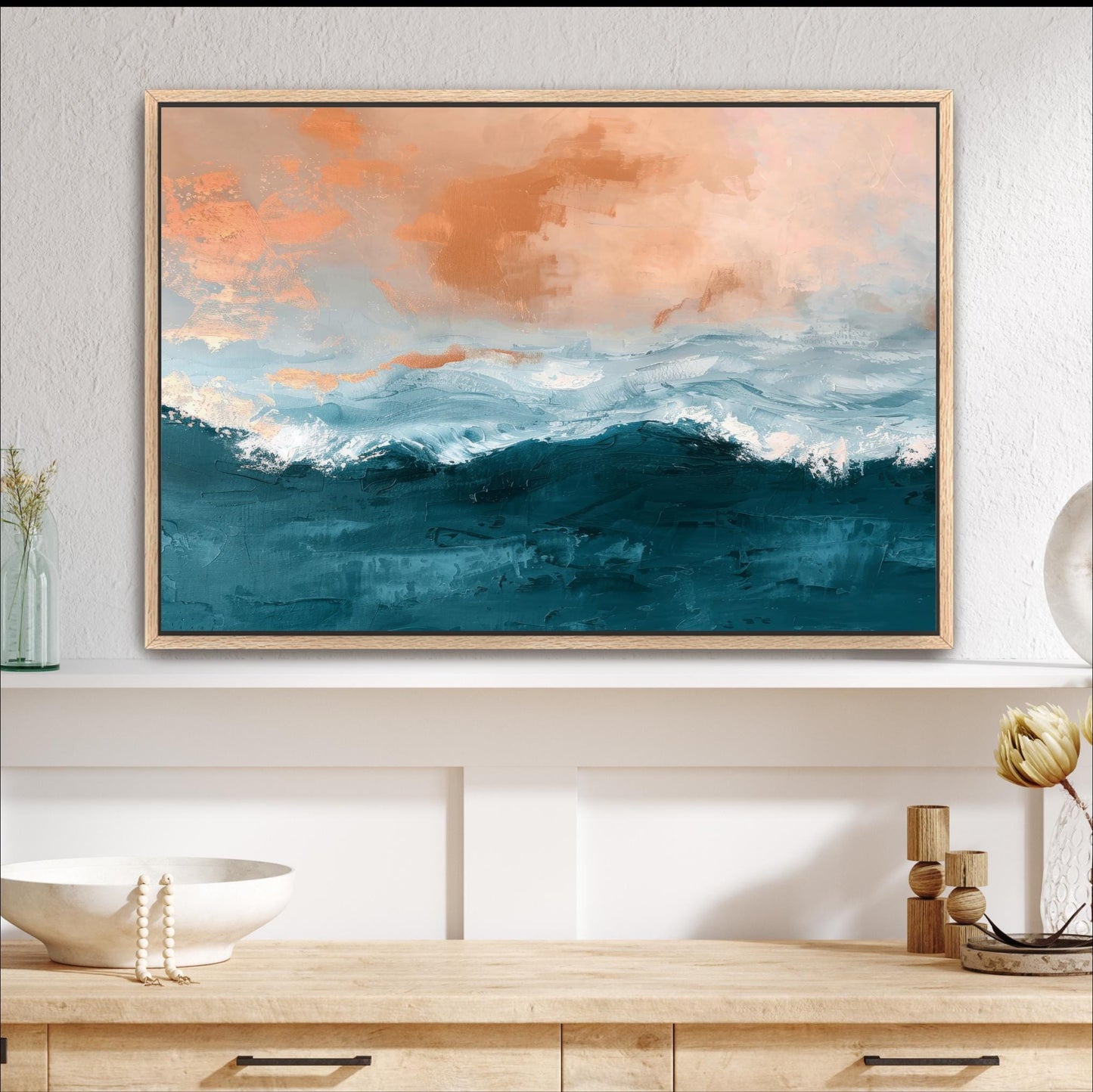 a large framed painting of a seascape with a blue and orange sky, depicting waves crashing against the shore. The painting is hung on a white wall above a wooden shelf, which also holds a white bowl, a vase with flowers, and a wooden sculpture.