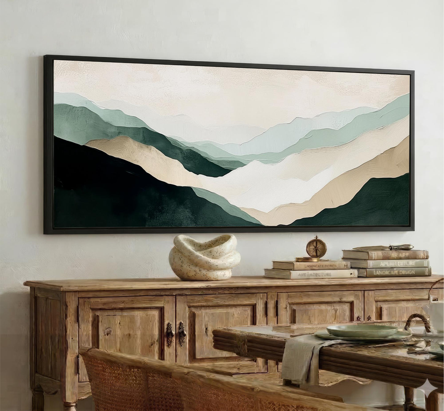 a large framed painting of mountains hanging on a wall above a wooden cabinet. The painting has a soothing color palette of green, blue, and beige, creating a serene and calming atmosphere in the room.