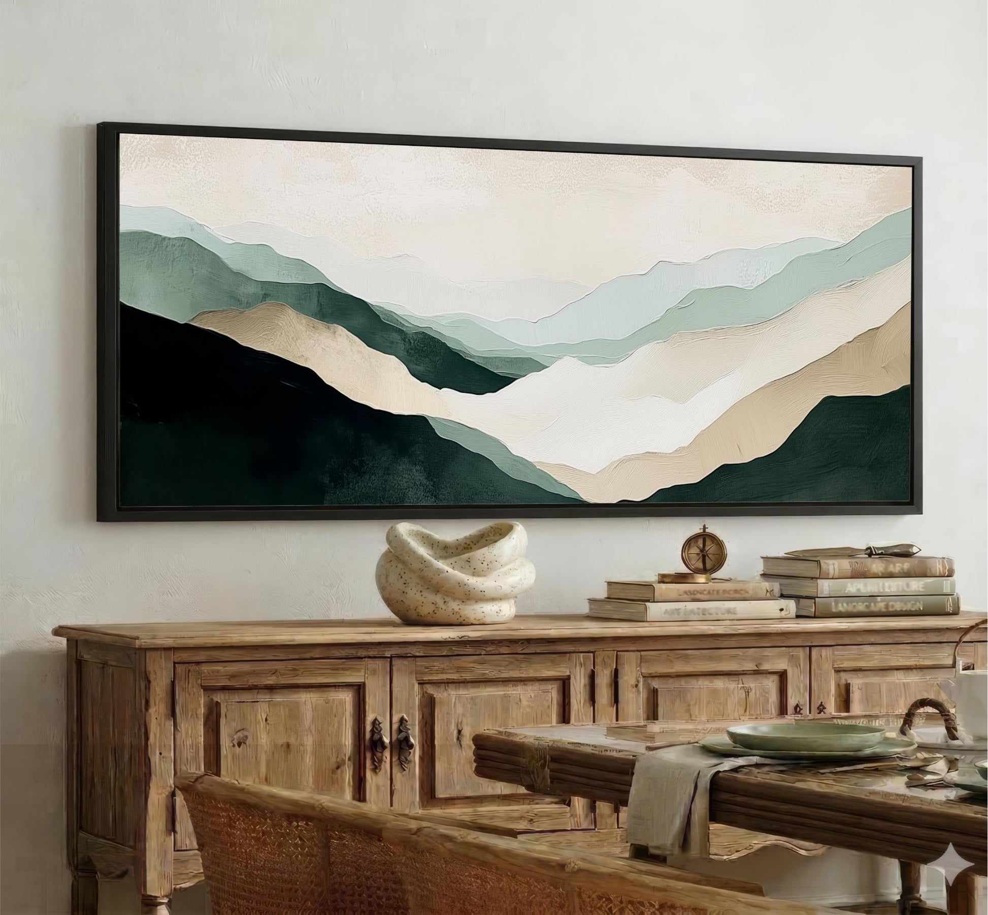 a large framed painting of mountains hanging on a wall above a wooden cabinet. The painting has a soothing color palette of green, blue, and beige, creating a serene and calming atmosphere in the room.