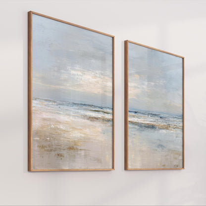 two framed paintings of a serene landscape, depicting a tranquil beach scene with a calm ocean and a cloudy sky.