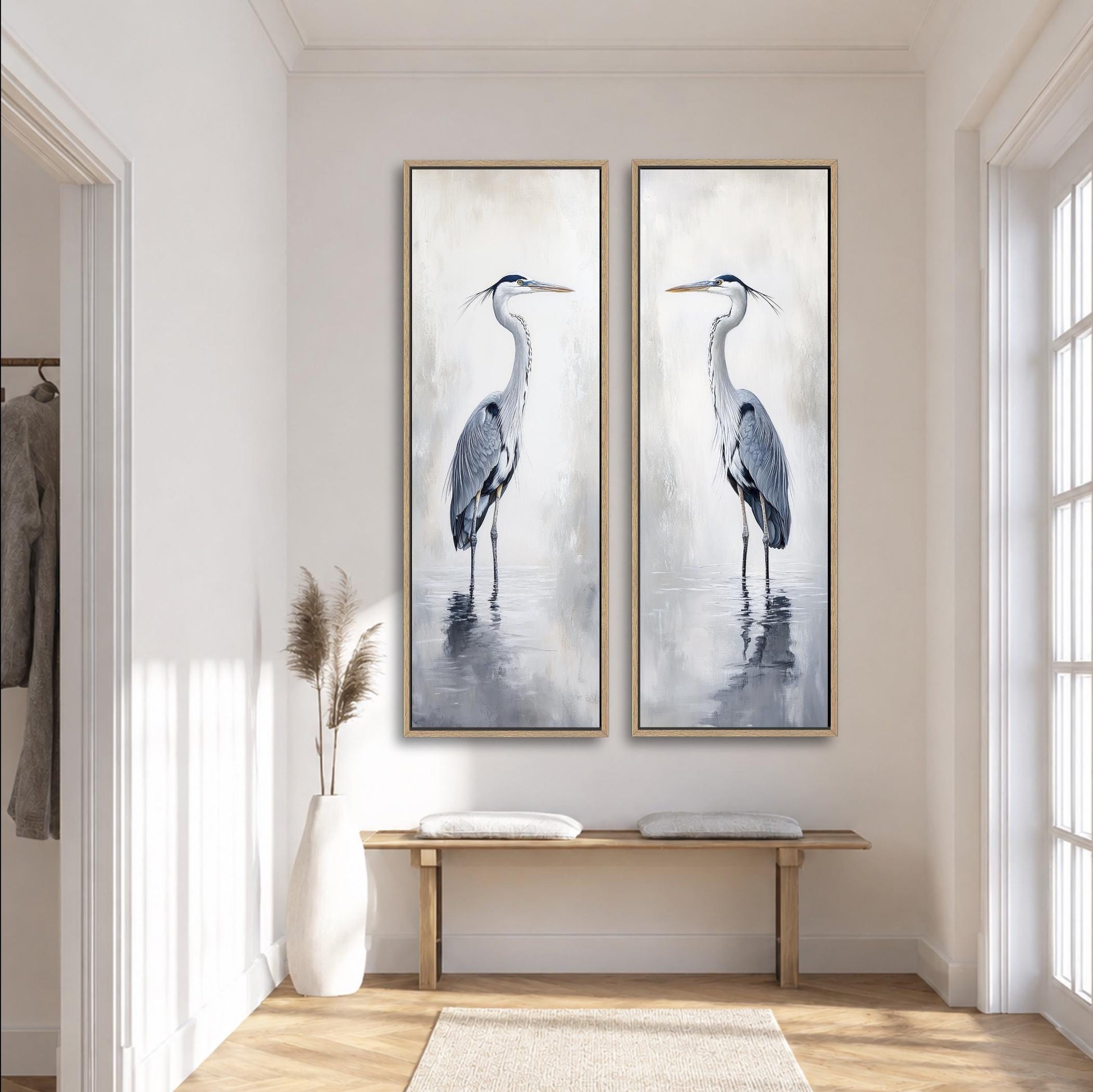 two large paintings of a tall bird, possibly a crane or heron, hanging on a white wall in a room with a wooden bench and a vase of dried plants.