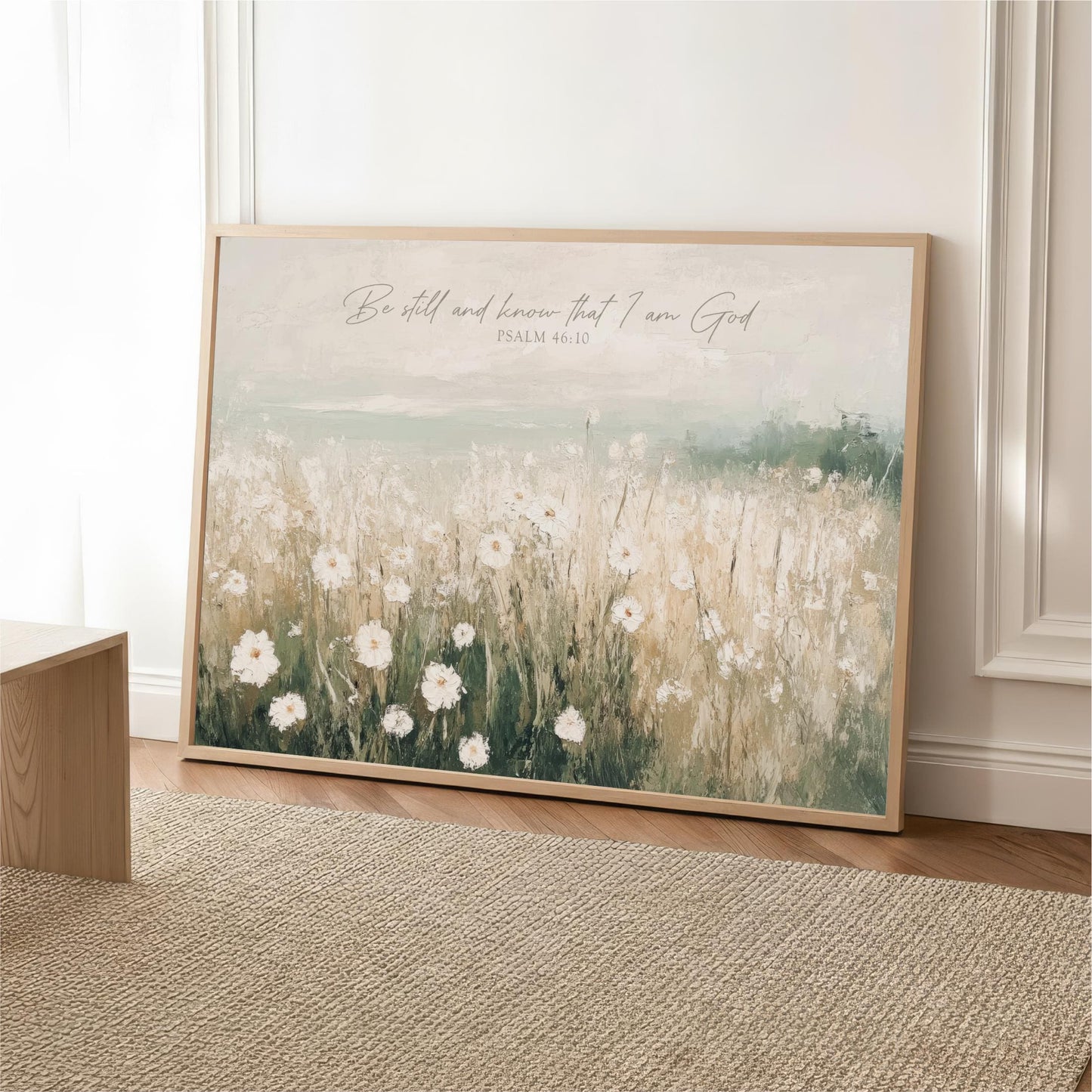 A framed painting of a field of white flowers is displayed on a wall, with a text overlay that reads "Be still and know that I am God" and " Psalm 46:10".