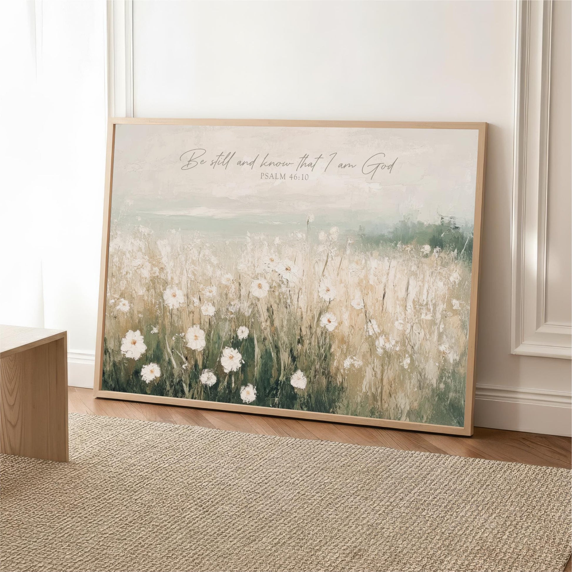 A framed painting of a field of white flowers is displayed on a wall, with a text overlay that reads "Be still and know that I am God" and " Psalm 46:10".